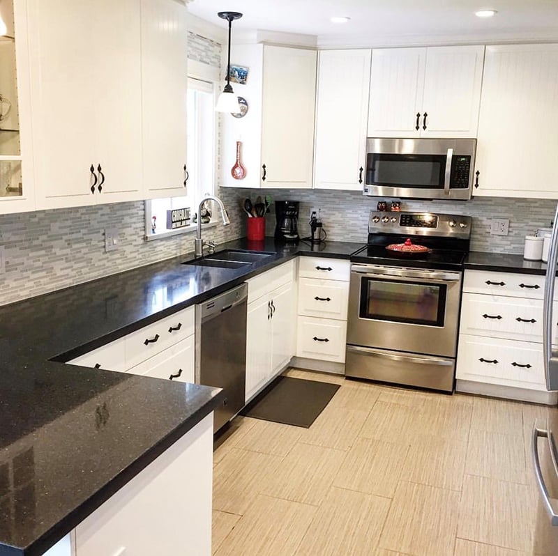 Modern kitchen renovation featuring white shaker cabinets, black quartz countertops, stainless steel appliances, and a stylish mosaic tile backsplash, designed by Sayers Contracting.