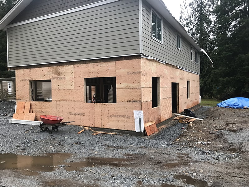 Home renovation and expansion project in progress, featuring a two-story house with newly framed lower-level walls, construction materials on-site, and a partially completed exterior, managed by Sayers Contracting.