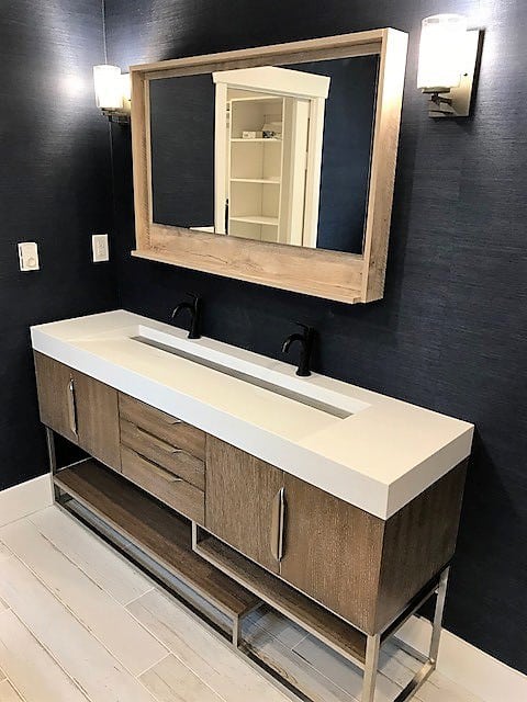 Modern bathroom renovation featuring a wooden double vanity with a white quartz countertop, matte black faucets, a matching wooden-framed mirror, and navy textured walls, designed by Sayers Contracting.