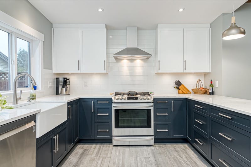 Stylish kitchen renovation featuring navy blue lower cabinets, white upper cabinets, a farmhouse sink, and stainless steel appliances, designed by Sayers Contracting.